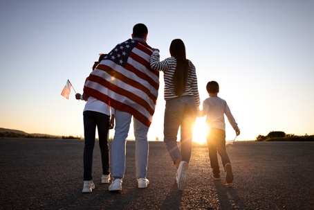 family facing the sunset while wearing US flag on their shoulders