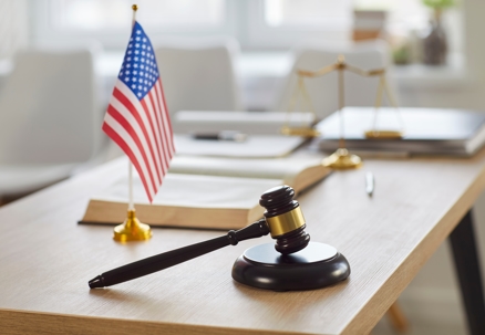 Closeup of modern office interior of judge or lawyer with wooden gavel and american flag on table. Empty courtroom with nobody at workplace. Justice, jurisdiction and legal law concept.